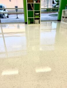 Pristine, mirror-polished VCT flooring reflecting vibrant green classroom walls and storage shelving during a return cleaning visit at a Houston childcare facility.